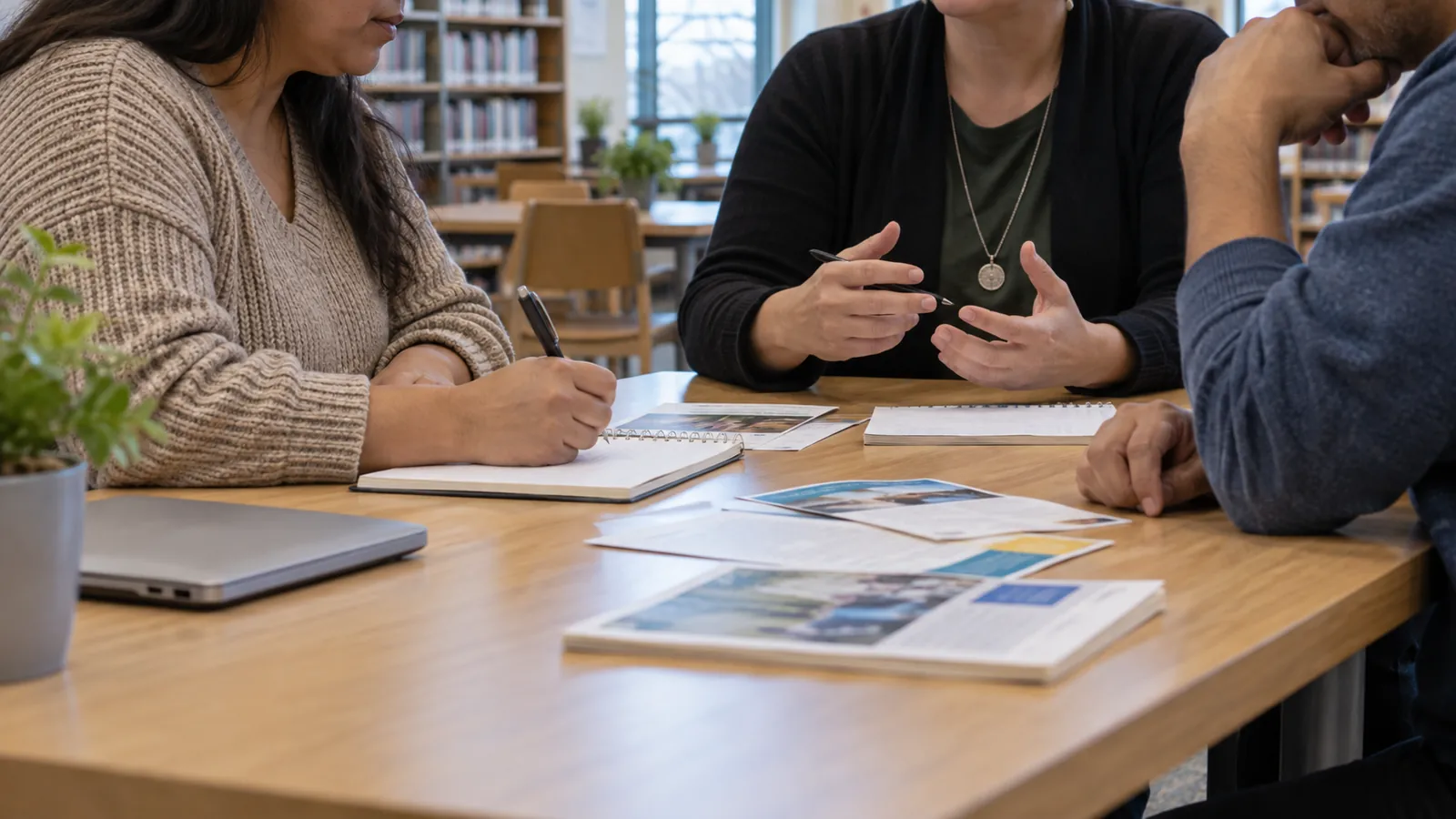 People discuss printed community information across a library table.