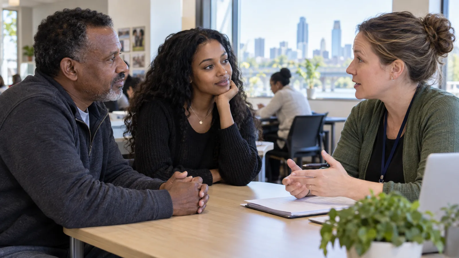 Three adults hold a thoughtful conversation around a table at a community center.