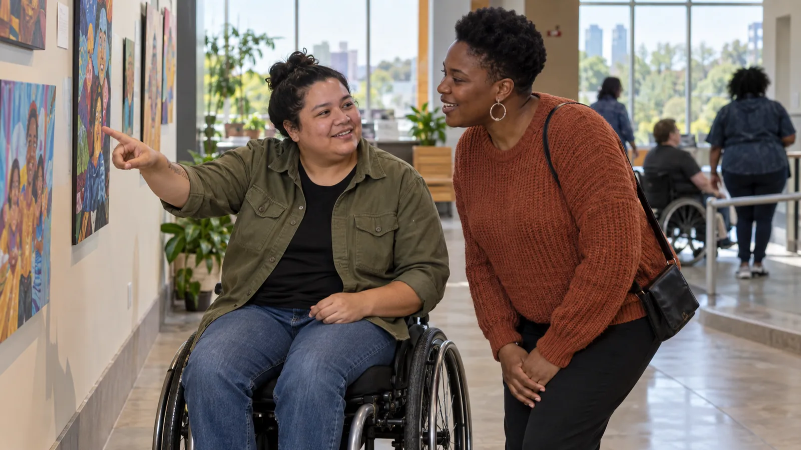 Two colleagues, one using a wheelchair, discuss artwork at a community center.