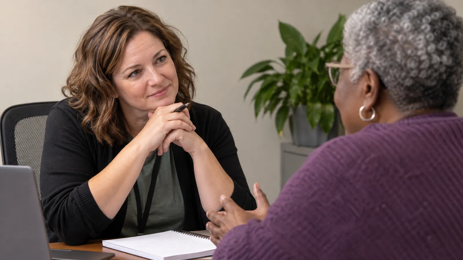 A staff member listens closely to an older visitor at a service desk.