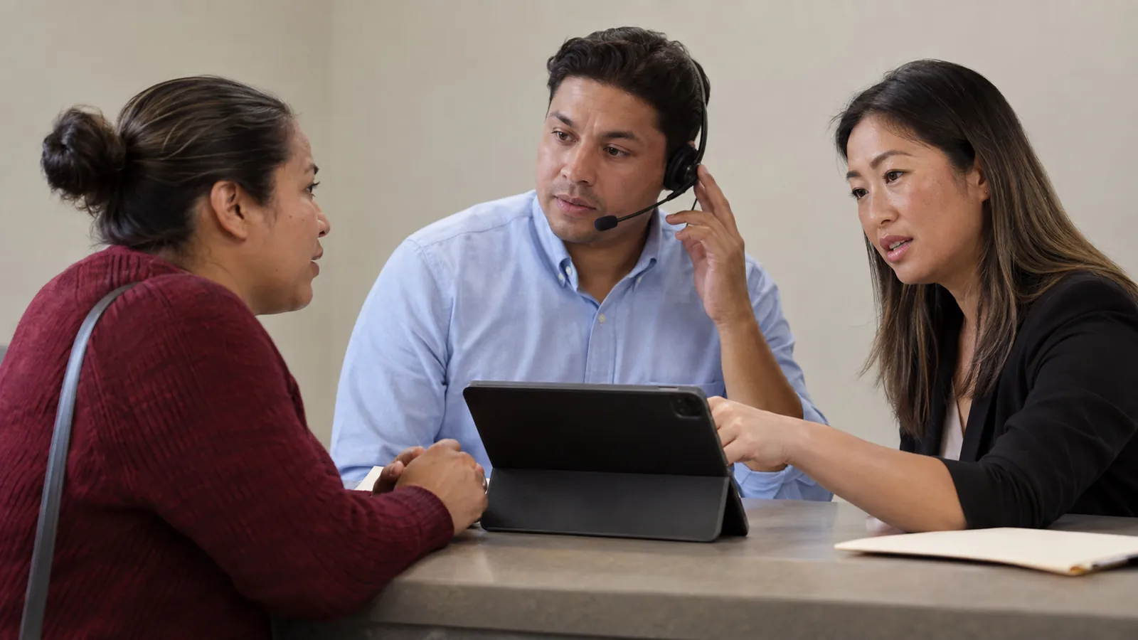 A visitor, interpreter, and navigator talk over a tablet at a counter.