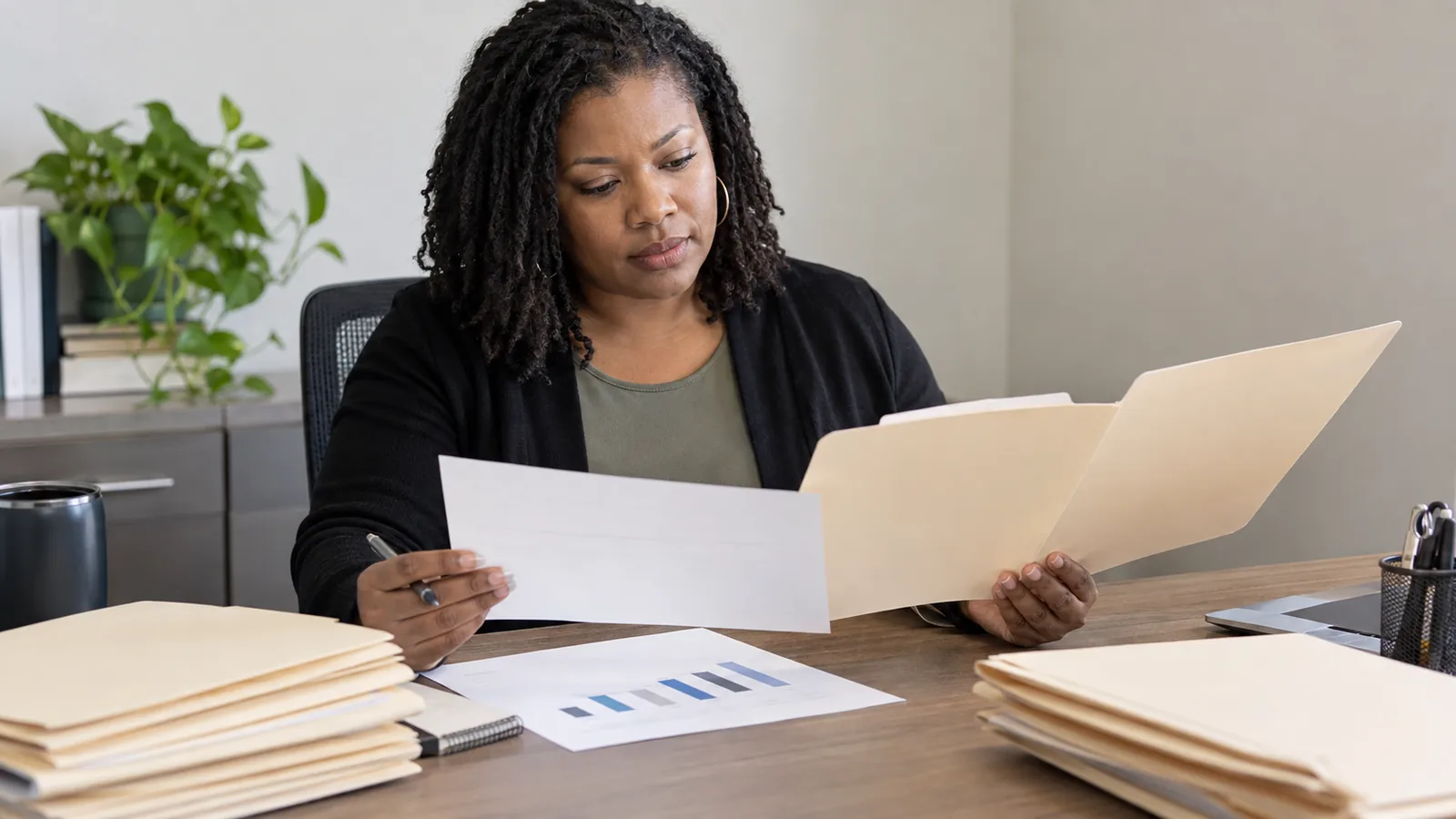 A reviewer studies documents and a simple chart at her desk.