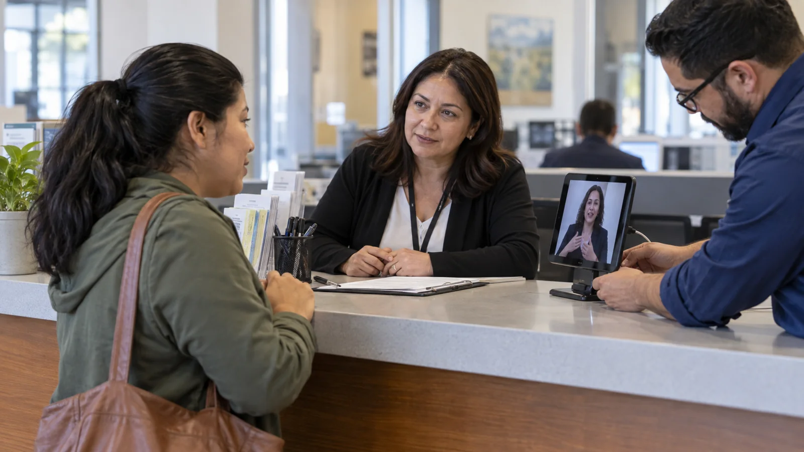 A visitor and staff member use a remote interpretation tablet at a service counter.